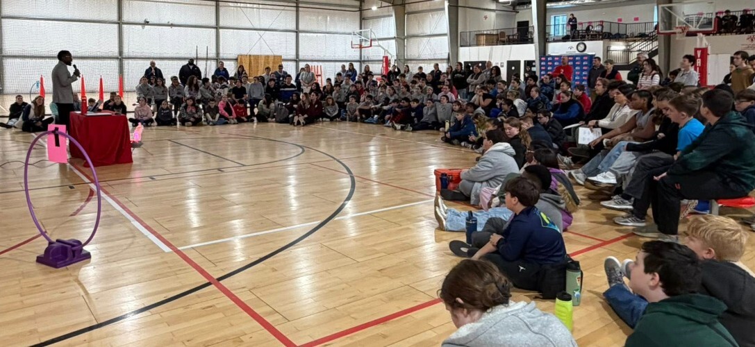 Speaker with microphone speaking to large group in gym