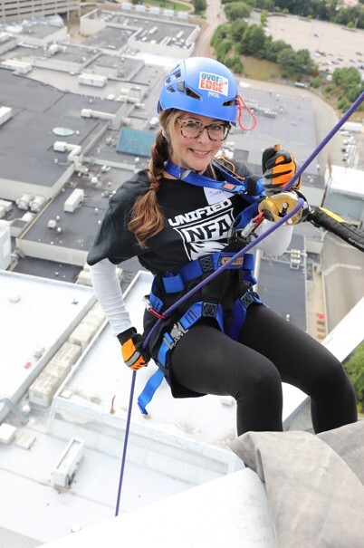 Woman smiles at camera while rappelling