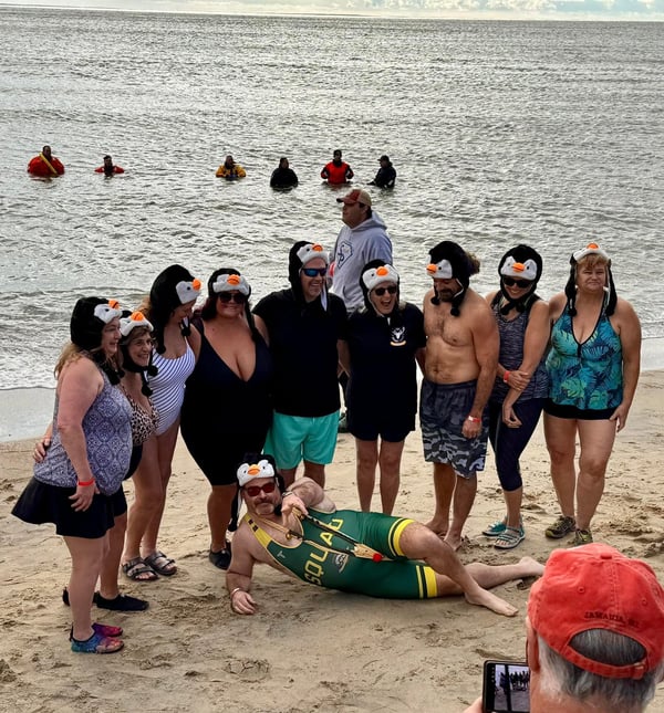 People dressed in penguin hats with bathing suits pose in front of ocean before Penguin Plunge